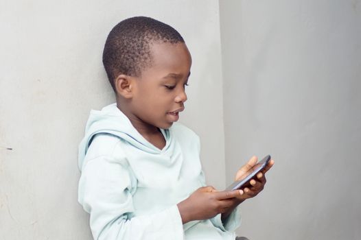 This little boy sitting against the wall manipulates a mobile phone with emotion.