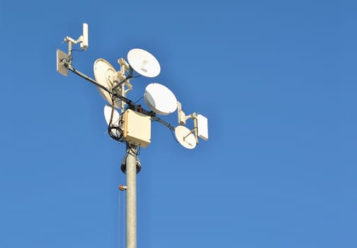 Antenna pylon with transmitters and satellites on blue sky background. 