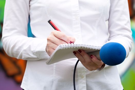 Female journalist at news conference, writing notes, holding microphone