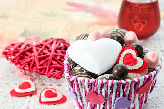 Colorful basket with sweets and biscuits on the table, decorative Valentine day heart candle holder. Selective focus.