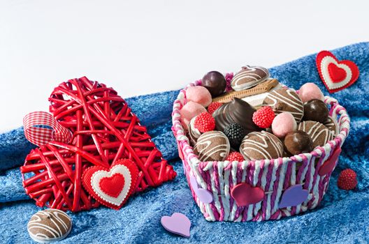 Candy basket, cookies and a decorative Valentines day hearts on blue velvet cloth and a white background. Selective focus.