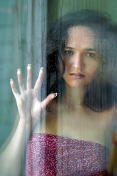 Woman with sad smile behind a wet window