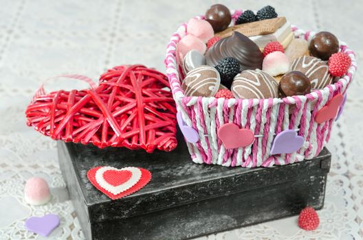 Candy basket, cookies and a decorative Valentines day heart on the old box. Selective focus.