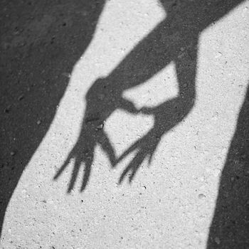 Two hands forming a heart shadow on the asphalt. Black and white photography