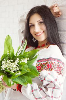 Portrait of a beautiful Ukrainian girl in national dress with bouquet of flowers lily of the valley