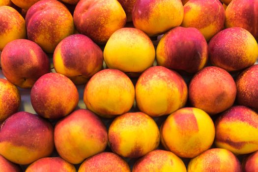 Background of a stacked yellow and red peaches close up. Yellow peaches pattern on sale at the market.