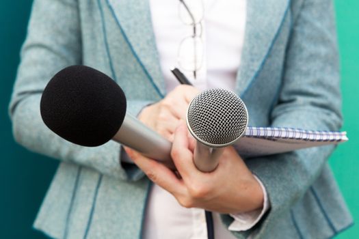 Female journalist at news conference, writing notes, holding microphone