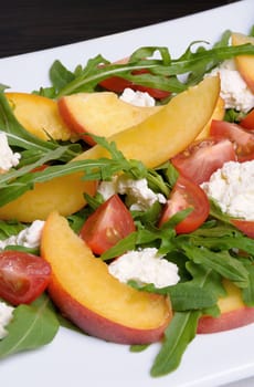 Salad with slices of peach, cherry tomatoes, arugula, feta