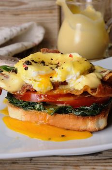Eggs Benedict with tomato, slices of bacon, spinach under hollandaise sauce on toast
