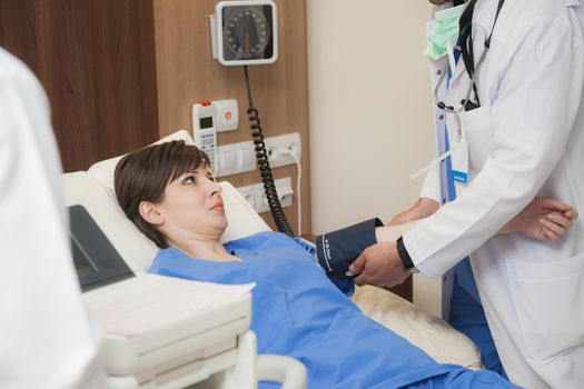 A doctor with white apron is measuring the blood pressure of a young female patient.