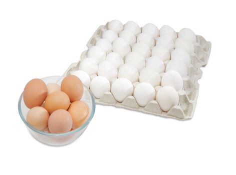 Fresh brown free-range eggs in a glass bowl and white chicken eggs in an egg tray from commercial factory farming on a light background
