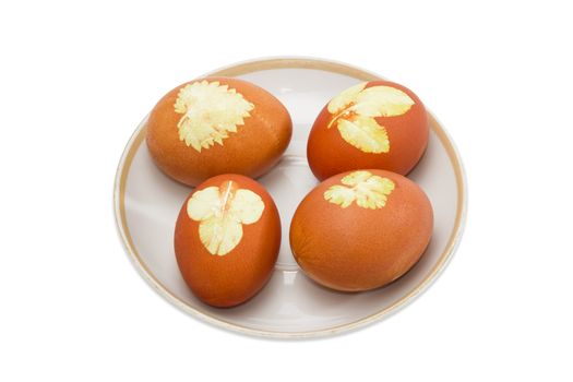 Several Easter eggs boiled with onion skins and leaf patterns on a saucer on a light background
