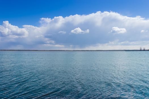 Fragment of the bay with water surface covered with ripples against the embankment and sky with clouds
