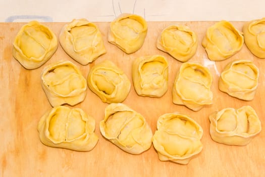 Uncooked manti (dumplings, meat dumplings) on a wooden cutting board during cooking 
