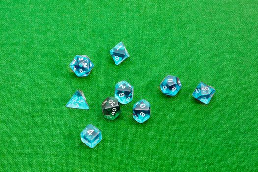 Set of blue and green specialized polyhedral dice with numbers used in role-playing games on a table with green cloth
