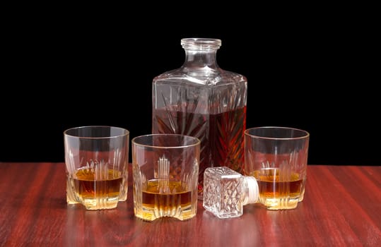 Decanter and three glasses with whiskey, stopper from the decanter on a wooden table on a dark background
