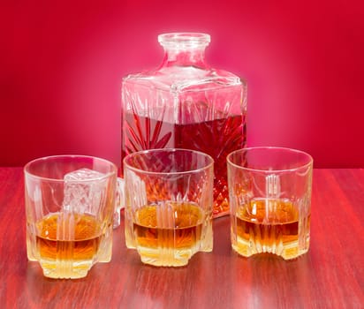 Decanter and three glasses with whiskey, stopper from the decanter on a wooden table on a red background
