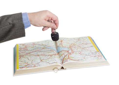 Male hand with car keys over an open old road atlas on a light background
