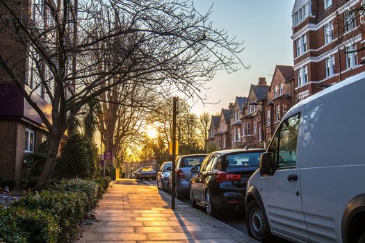 Beautiful picture of the sunset in London suburbs, taken in the side walk with trees, cars and tipical flats showing