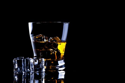 A glass of whiskey with ice on a black background