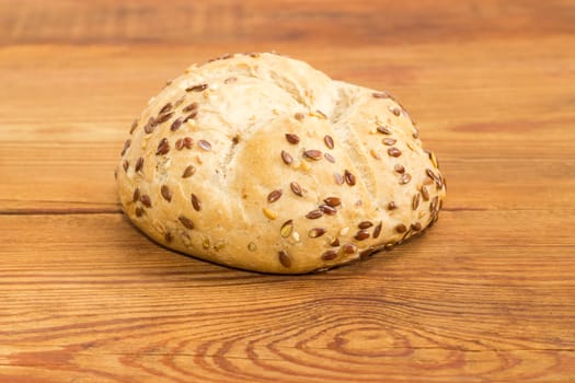 Round wheat sourdough bun, sprinkled with flax and sesame seeds on an old wooden surface
