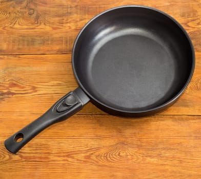 Modern cast frying pan, made of aluminum alloy with ceramic non-stick coating and removable handle on an old wooden surface
