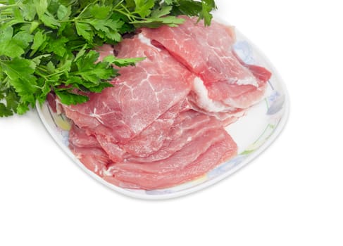 Sliced fresh chilled pork on a dish closeup against the background of bunch of parsley on a light background 
