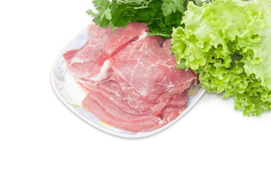 Sliced fresh chilled pork on a dish closeup against the background of bunch of parsley and lettuce on a light background 
