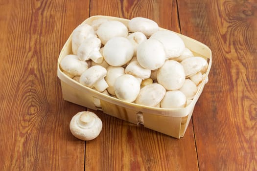 Fresh cultivated button mushrooms in the wooden basket and one mushroom separately beside on an old wooden surface
