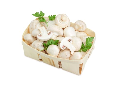 Fresh cultivated common button mushrooms and twigs of parsley in the wooden basket on a light background 
