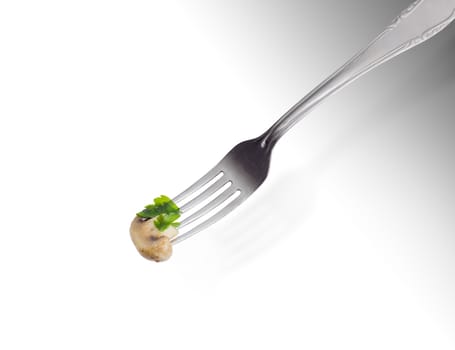 Half of the fried button mushroom with parsley leaf on the stainless steel fork on a light background
