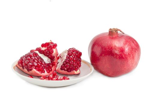 One whole ripe pomegranate and part of the fresh split pomegranate on a saucer on a light background
