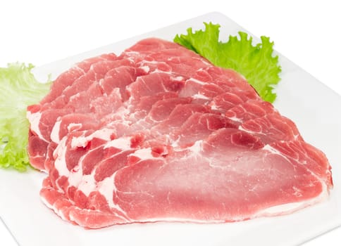 Sliced fresh chilled pork loin with lettuce leaves on a white dish closeup on a light background 
