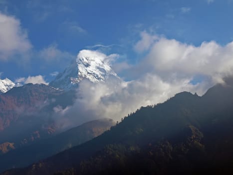 Mountain peak covered with glaciers against the backdrop of mountain ranges and the sky with clouds in the morning in the Himalayas
