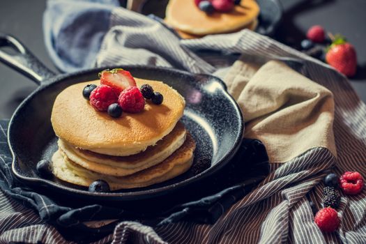 Home made pancakes with berries on metal frying pan decorated with berries (blueberries, raspberries and blackberries). Top View.