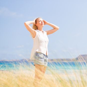 Relaxed woman enjoying sun, freedom and life an a beautiful beach. Young lady feeling free, relaxed and happy. Concept of vacations, freedom, happiness, enjoyment and well being.