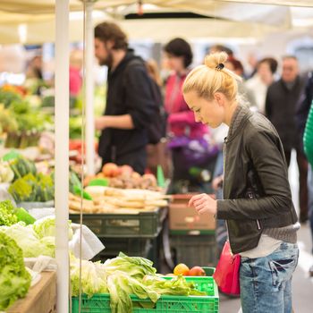 Woman buying fruits and vegetables at local food market. Market stall with variety of organic vegetable.