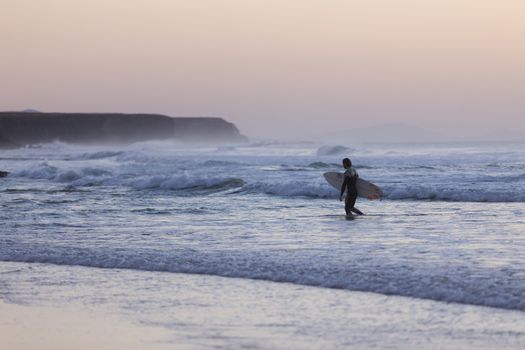 Male surfers on beach with surfboard at dusk at El Cotillo beach, famous surfing destination on Fuerteventura, Canary Islands, Spain. Panoramic composition.