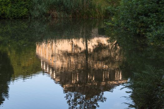 Reflection of a building in the water surface of a small pond.