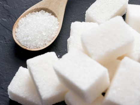 background of sugar cubes and sugar in spoon. White sugar on black background. Sugar cubes and granulated in wooden spoon