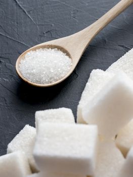 background of sugar cubes and sugar in spoon. White sugar on black background. Sugar cubes and granulated in wooden spoon