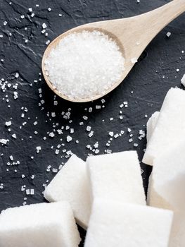 background of sugar cubes and sugar in spoon. White sugar on black background. Sugar cubes and granulated in wooden spoon