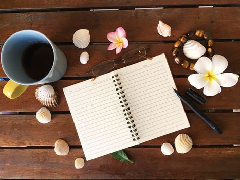 Top view mock up of open notebook, pen, cup of tea, seashells and flower on wooden table.