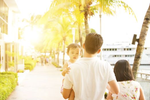 Rear view of young family enjoying outdoor activity together, walking in beautiful sunset during holiday vacation, outside the resort.