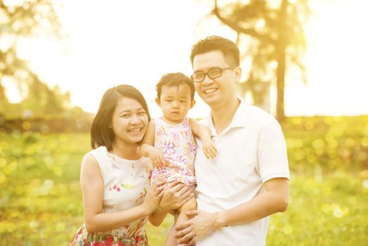 Portrait of happy family enjoying outdoor activity together, walking on garden park in beautiful sunset during holiday vacations.