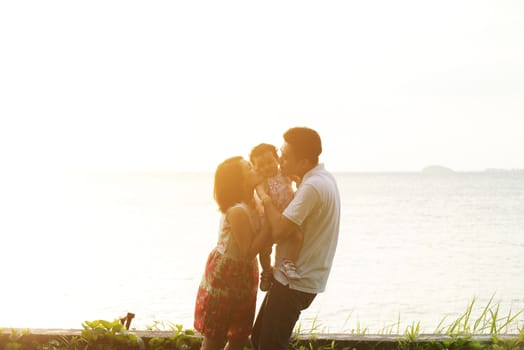 Happy family enjoying outdoor activity together, standing on coastline in beautiful sunset during holiday vacations.