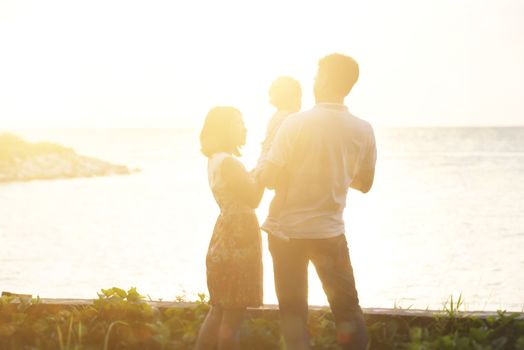 Happy Asian family enjoying outdoor activity together, standing on coastline in beautiful sunset during holiday vacations.
