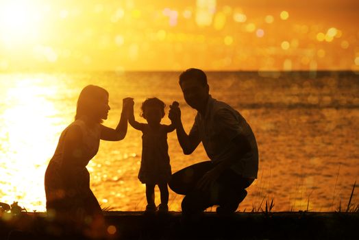Silhouette of Asian family outdoor activity, enjoying holiday together on coastline in beautiful sunset during vacations.