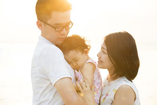 Young Asian family outdoor portrait, enjoying holiday together on seaside in beautiful sunset during vacations.