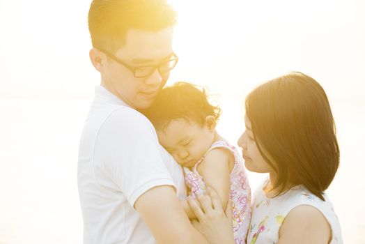 Young Asian family outdoor portrait, enjoying holiday together on coastline in beautiful sunset during vacations.